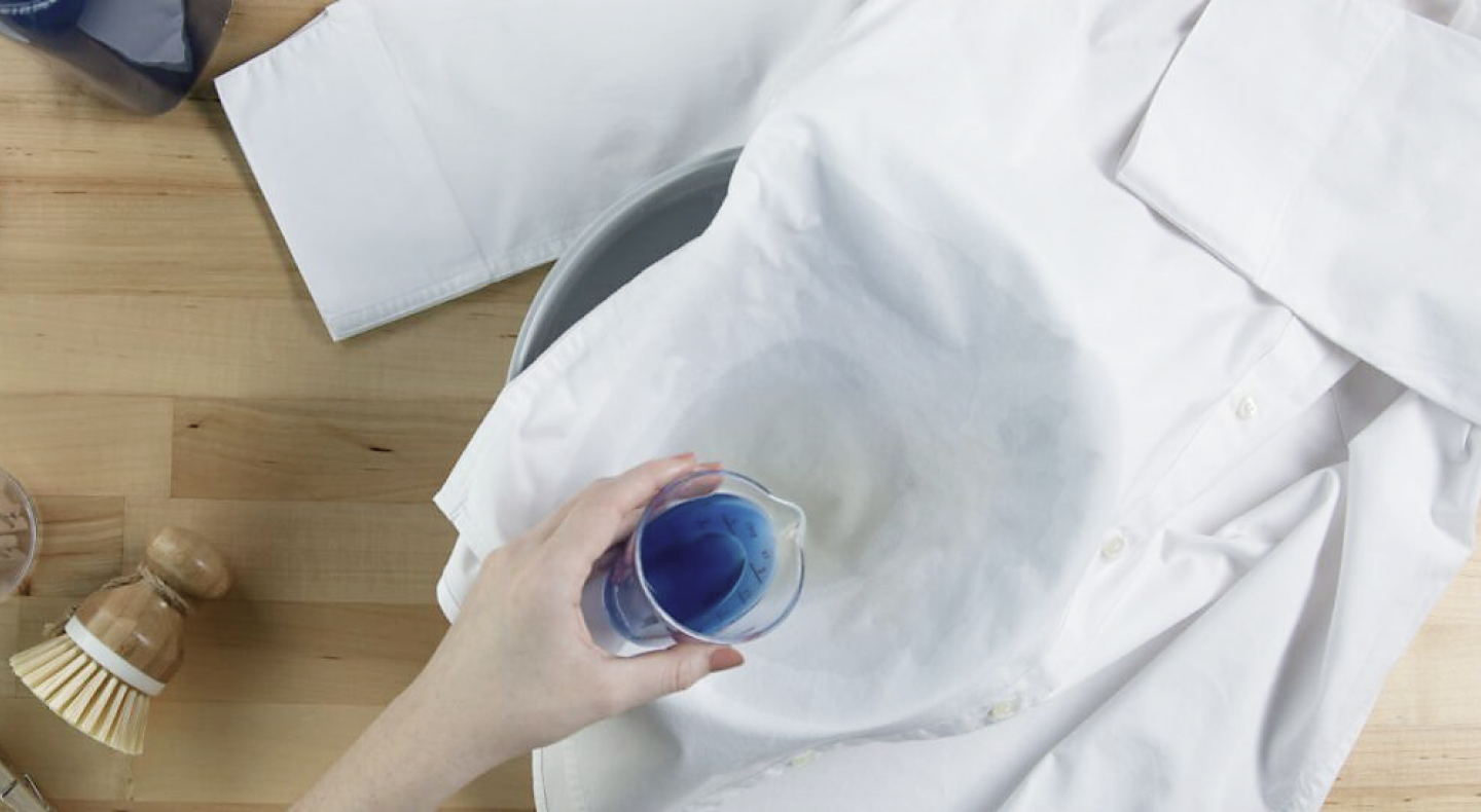 Hand pouring detergent to treat a stain on a button-front shirt Hand pouring detergent to treat a stain on a button-front shirt