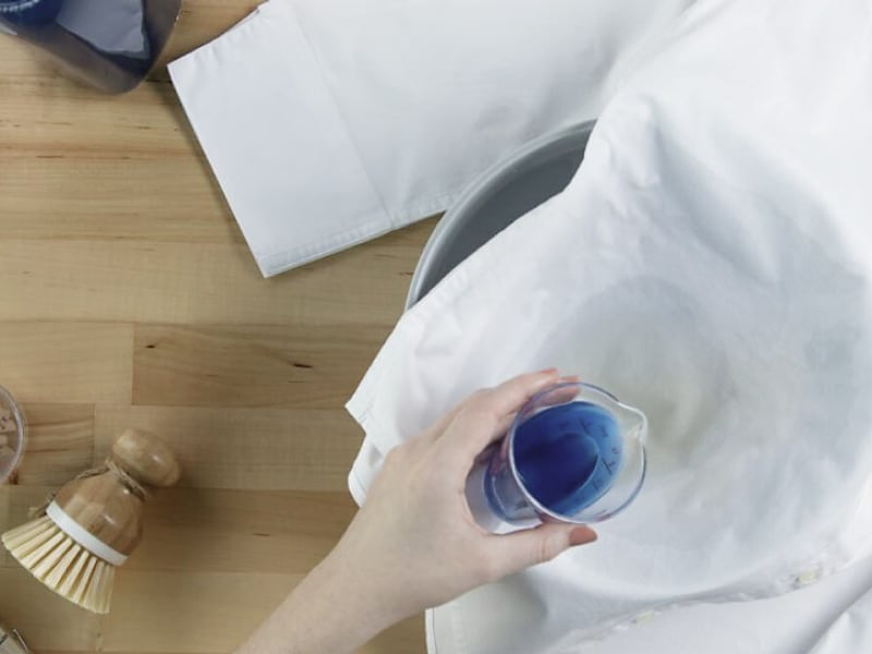 Hand pouring detergent to treat a stain on a button-front shirt Hand pouring detergent to treat a stain on a button-front shirt
