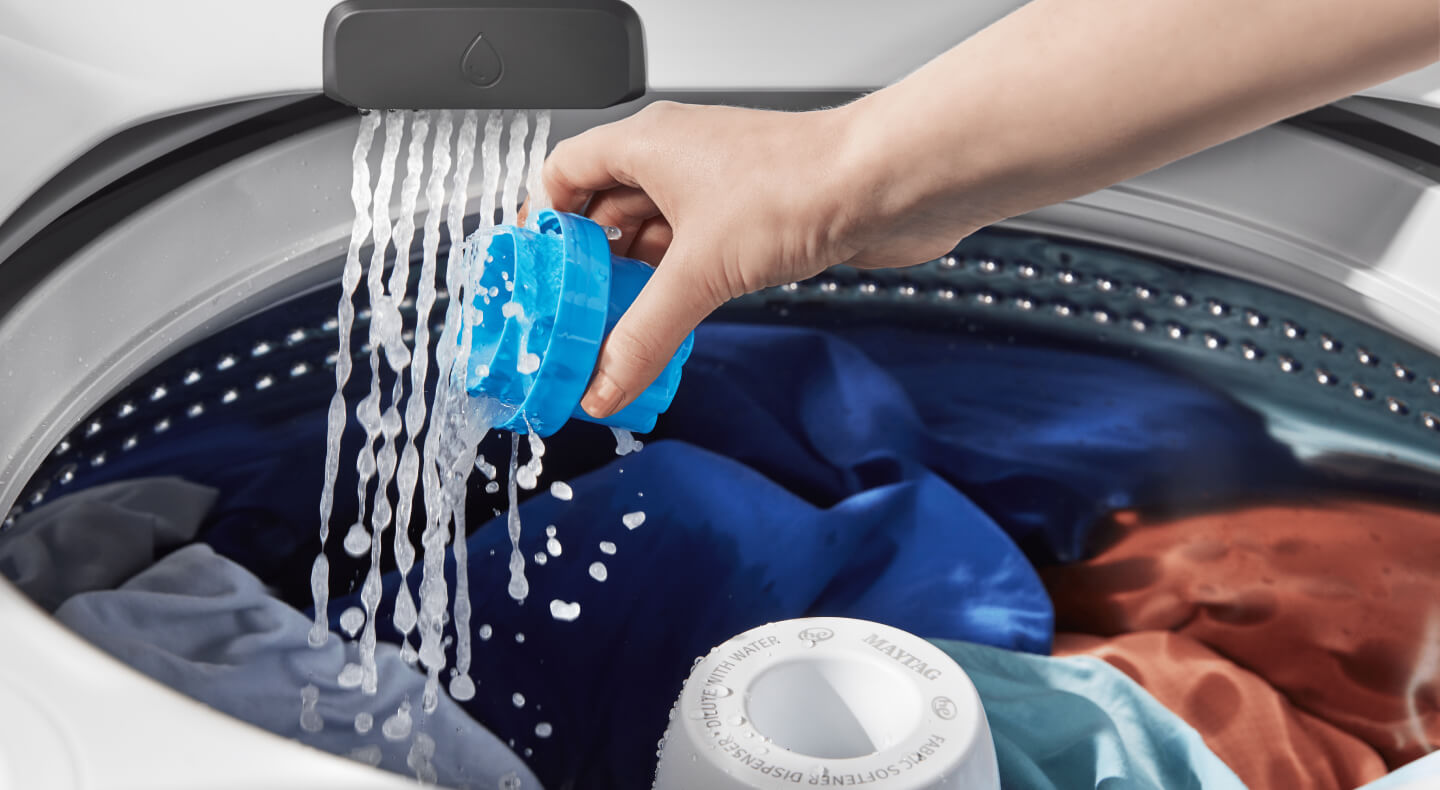 Person rinsing a detergent cap inside the washing machine Person rinsing a detergent cap inside the washing machine