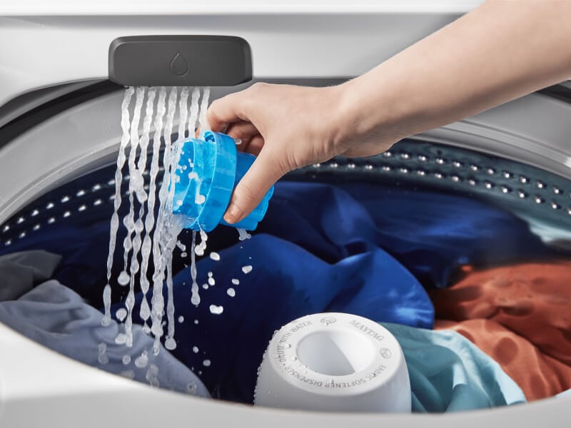 Person rinsing a detergent cap inside the washing machine Person rinsing a detergent cap inside the washing machine