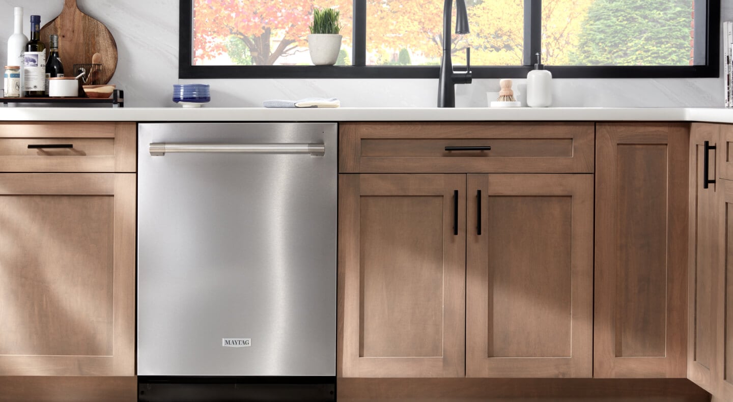 A stainless steel Maytag® dishwasher surrounded by brown cabinetry