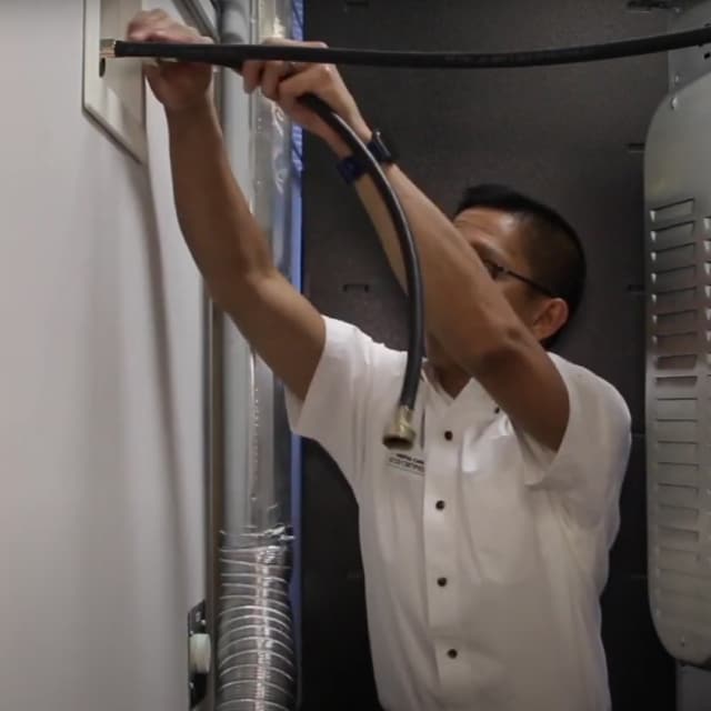 A man attaches a water inlet hose to a cold water inlet