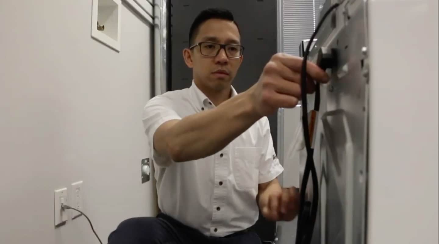 Person unplugging the power cord from the back of a washer.