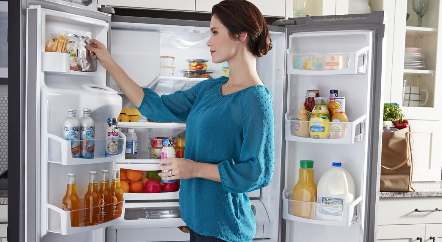 A person taking an item out of the top shelf of a refrigerator