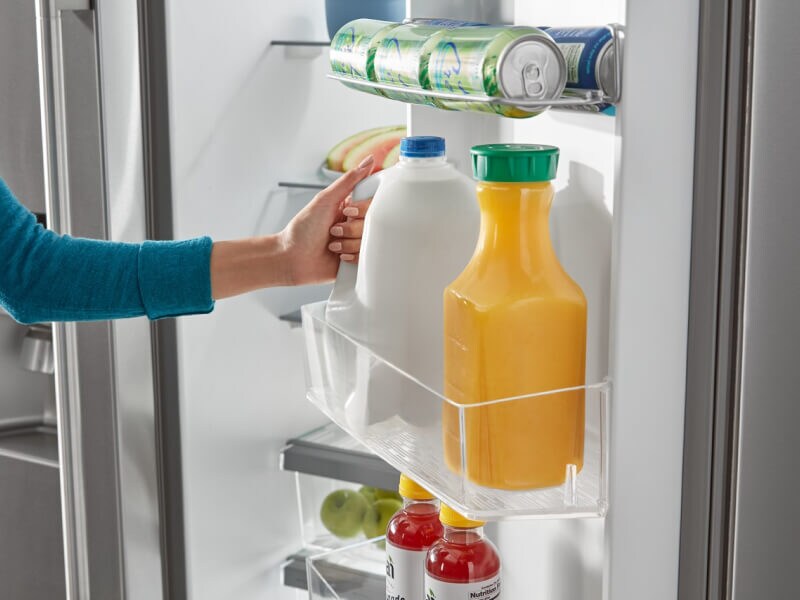 Person placing a jug of milk in a refrigerator door bin