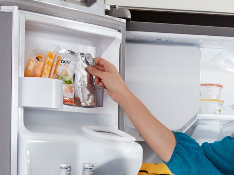 A person storing items in a fridge door shelf