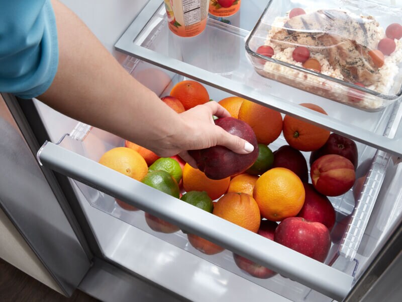 A person storing apples in a fridge crisper drawer