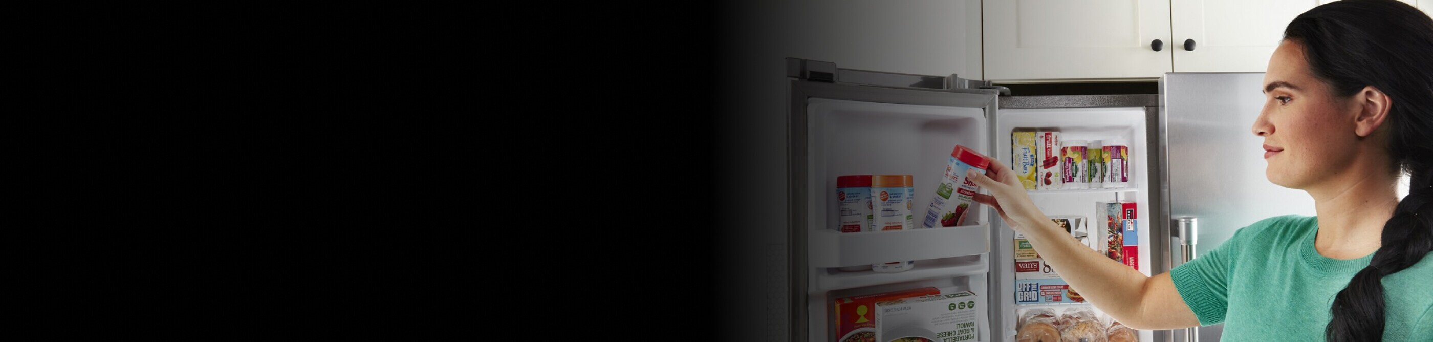 A person storing a container of fruit in a side-by-side refrigerator door