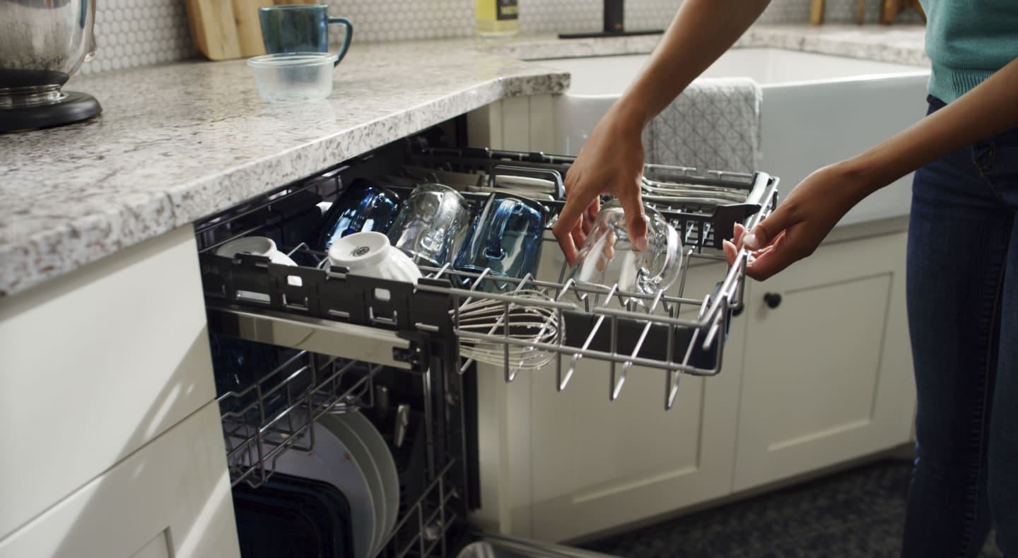 Person loading a glass cup into a dishwasher. Person loading a glass cup into a dishwasher.