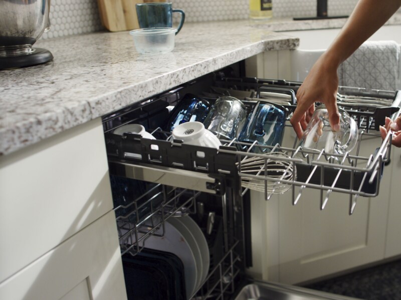 Person loading a glass cup into a dishwasher. Person loading a glass cup into a dishwasher.