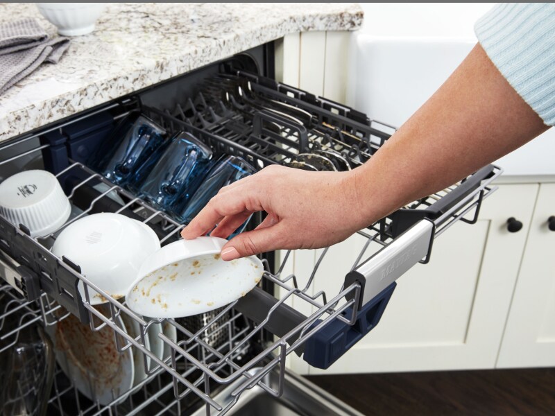 Person loading a dirty bowl into a dishwasher. Person loading a dirty bowl into a dishwasher.