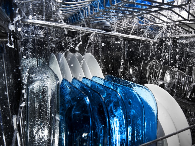 Plates and silverware being cleaned inside a dishwasher.