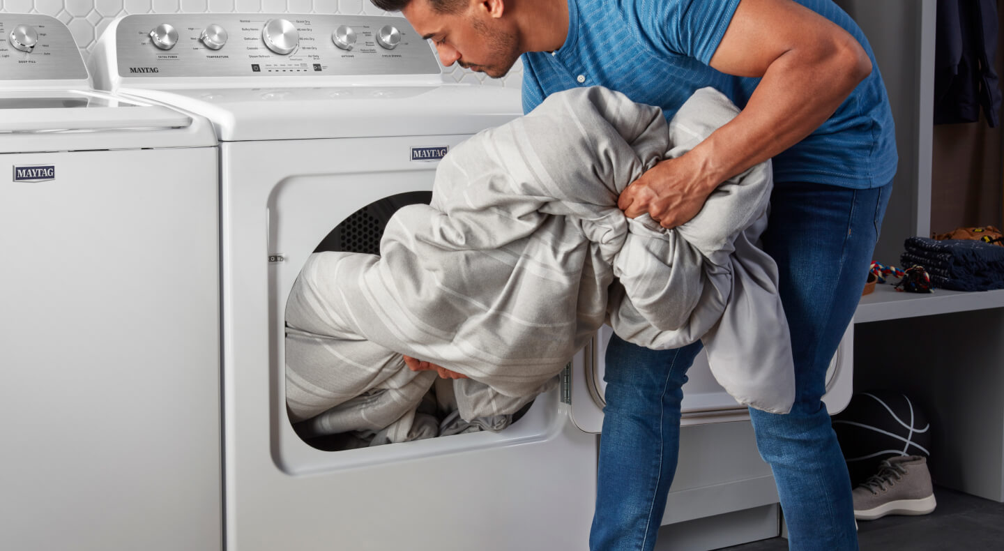 A person pulling a comforter out of a Maytag® dryer