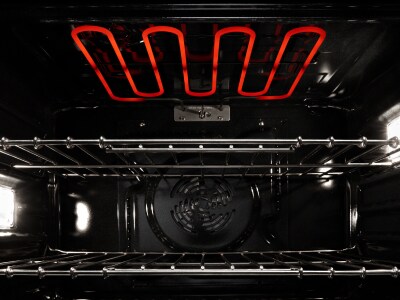 Interior of an oven with two racks and a broiler, which is lit up in orange