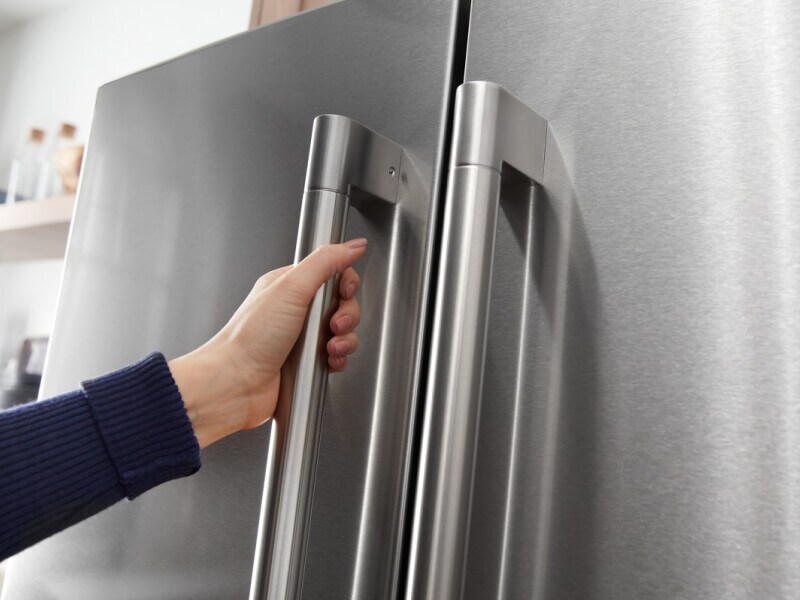 A hand shown opening a refrigerator door