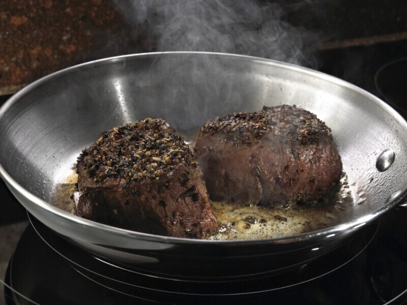 Two pieces of steak searing in a hot pan