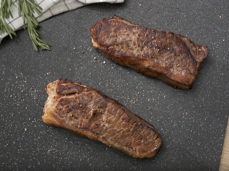 Two pieces of cooked steak resting on a cutting board
