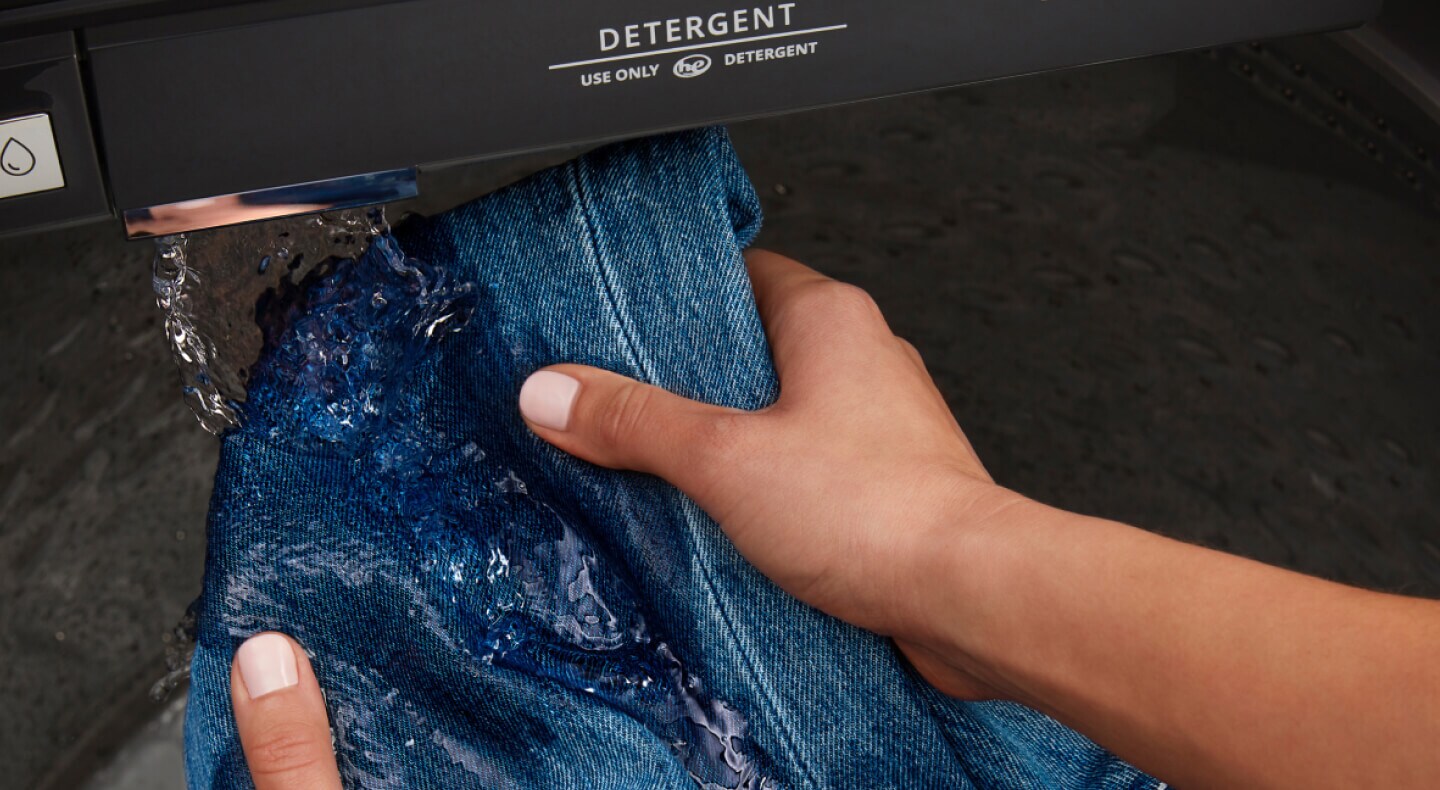 Person washing a pair of jeans with a Maytag® washing machine with Built-In Water Faucet
