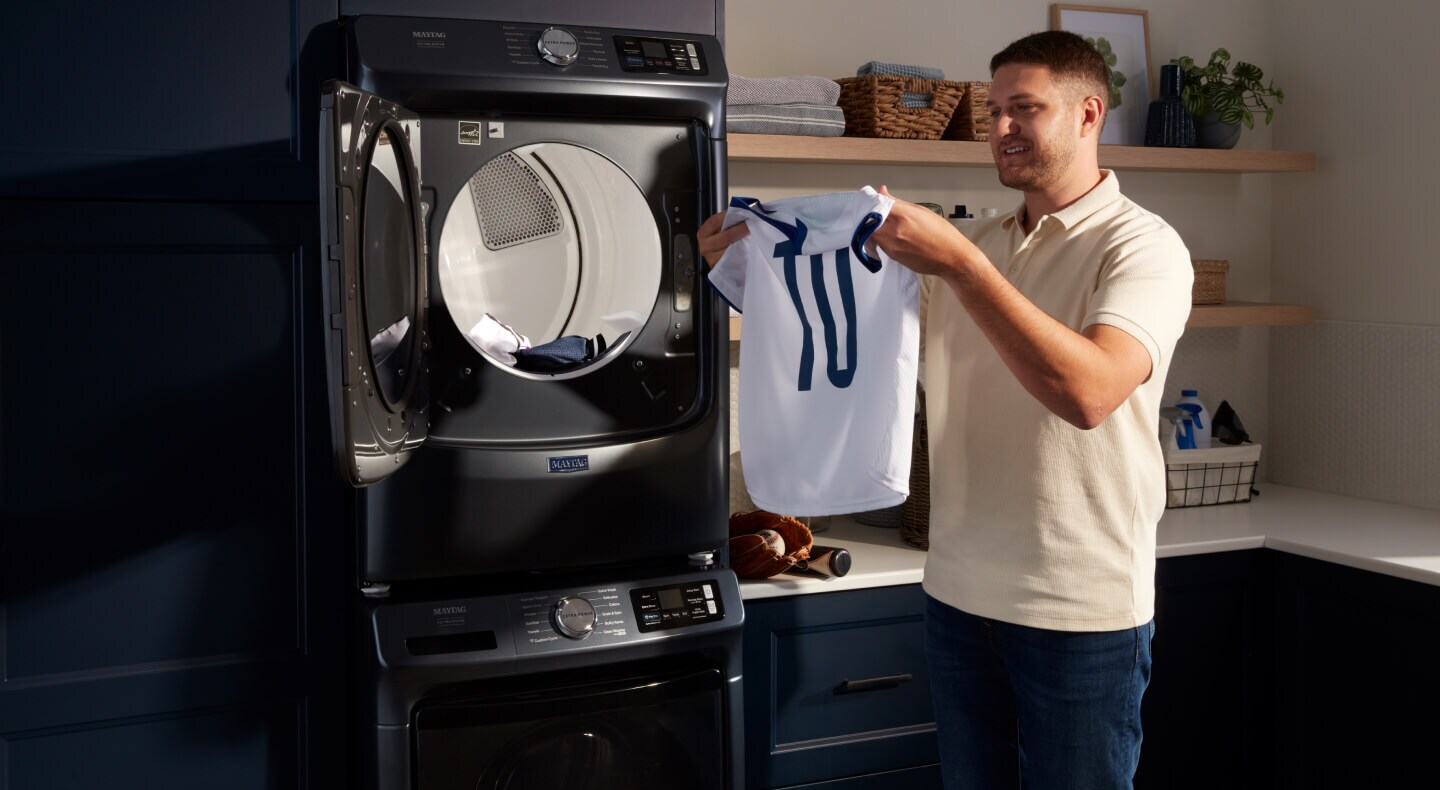 Person unloading jersey from stacked Maytag® washer and dryer pair