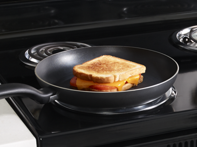 A grilled cheese sandwich in a frying pan on an electric stove with coil burners. A grilled cheese sandwich in a frying pan on an electric stove with coil burners.