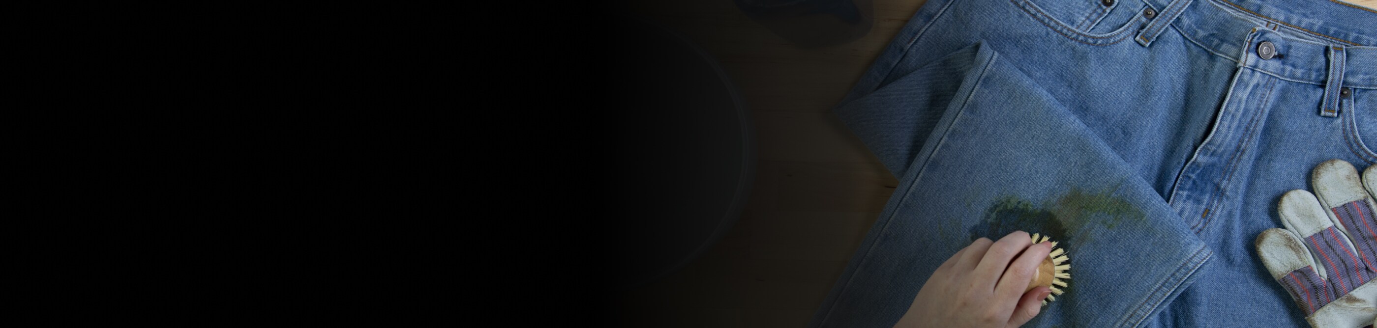 A hand scrubbing a grass stain on a pair of jeans