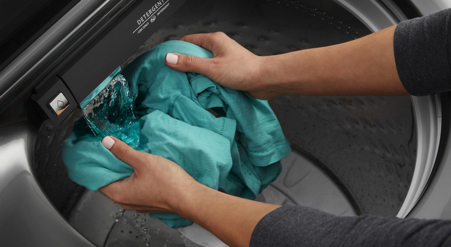 Person using built-in faucet in washing machine to rinse garment
