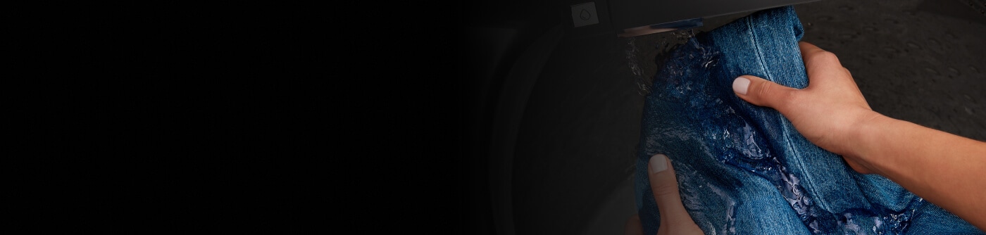 Person washing denim jeans under the built-in water faucet in a Maytag® washer