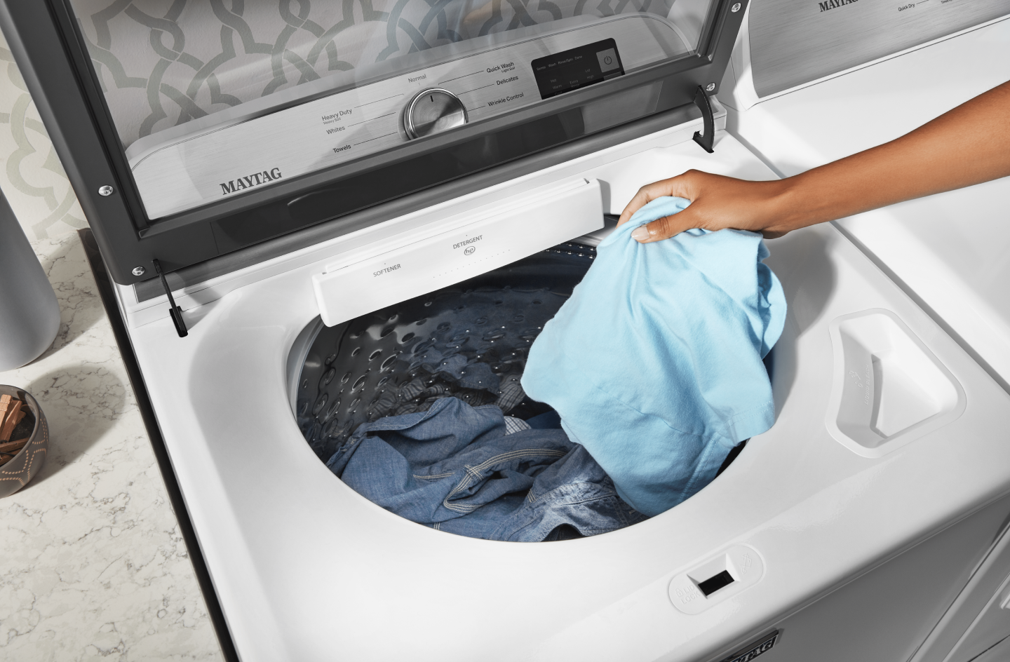 Person putting blue piece of clothing in the washer Person putting blue piece of clothing in the washer