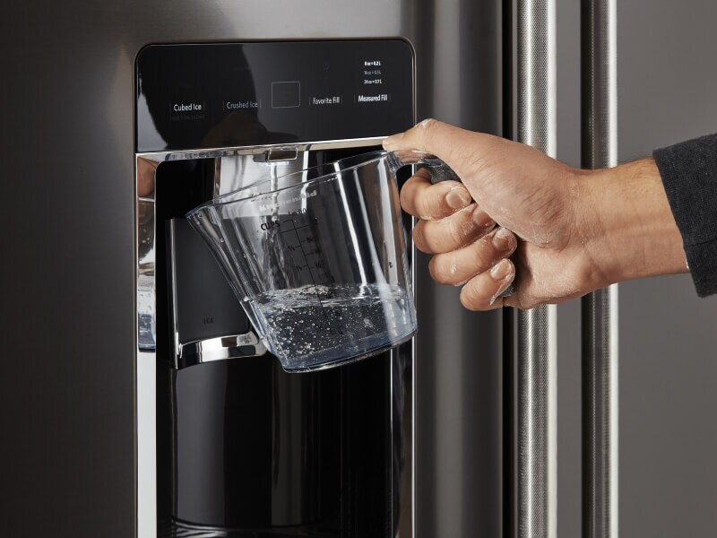 Person filling a large container with water from their refrigerator Person filling a large container with water from their refrigerator