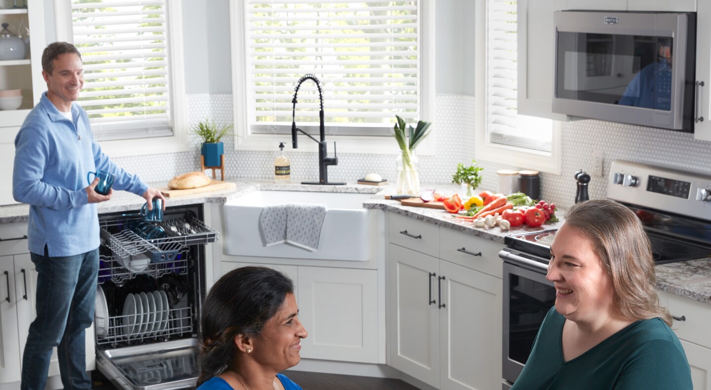 Multiple people in a kitchen with a man emptying a dishwasher