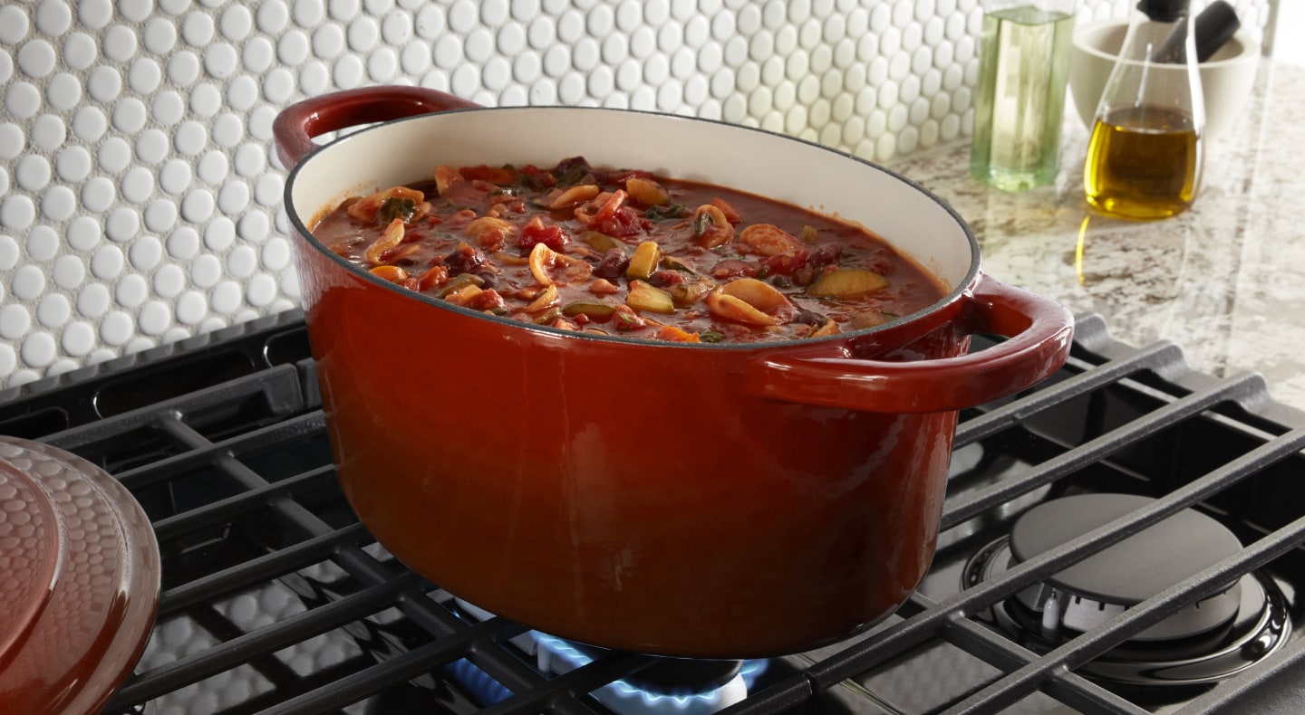 Red dutch oven full of stew simmering above gas burner Red dutch oven full of stew simmering above gas burner