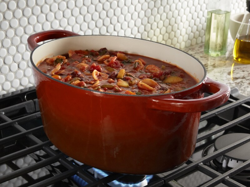 Red dutch oven full of stew simmering above gas burner Red dutch oven full of stew simmering above gas burner