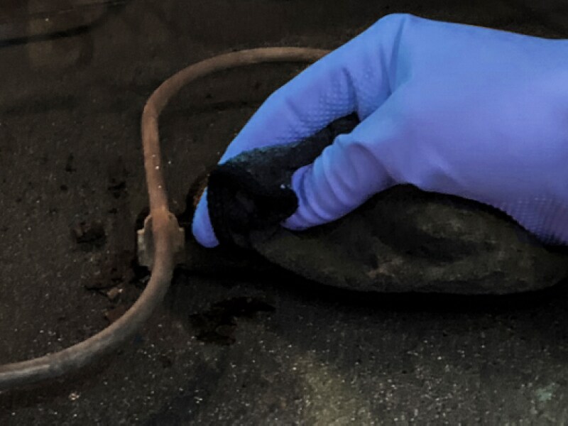 Close-up of hand in blue glove cleaning around heating coils of oven cavity