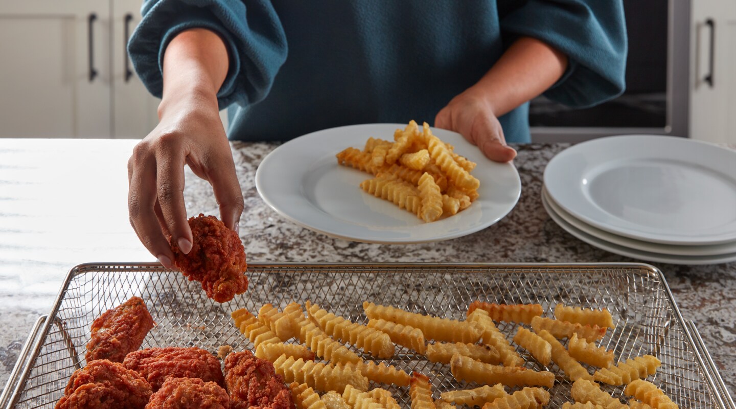 Person removing food from air fryer basket and placing on a plate