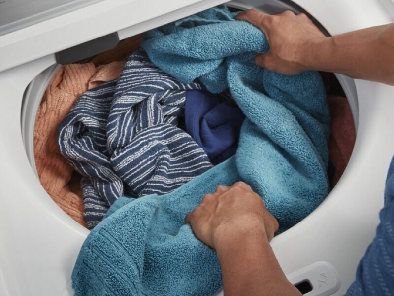 A person adding towels to a Maytag® top load washer