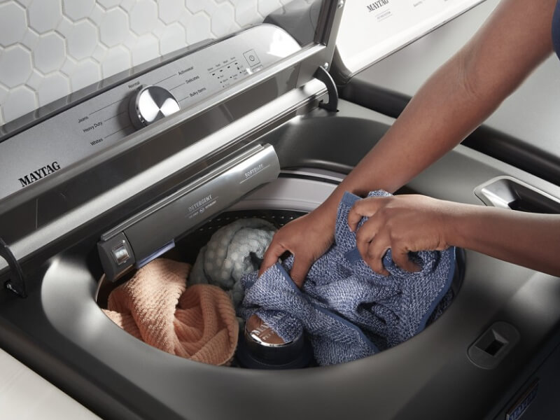 A person adding laundry to a Maytag® top load washer