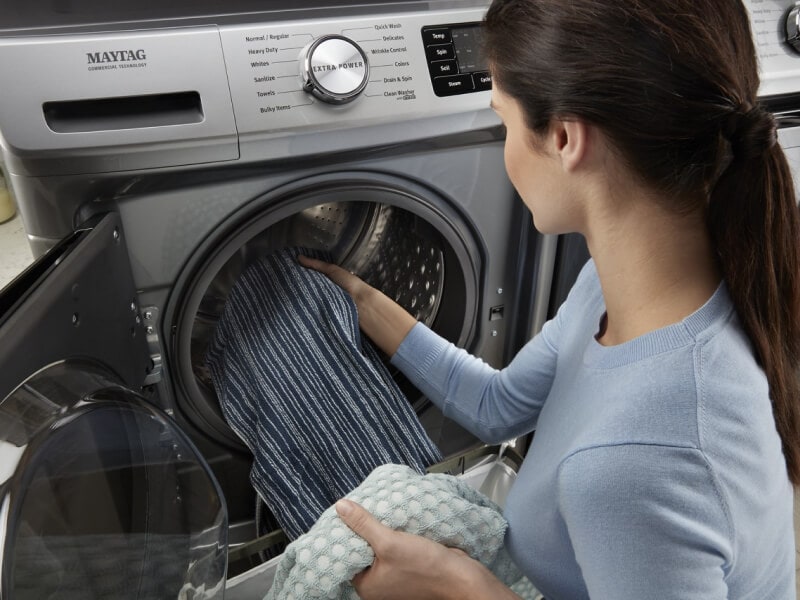 A person adding laundry to a Maytag® front load washer A person adding laundry to a Maytag® front load washer