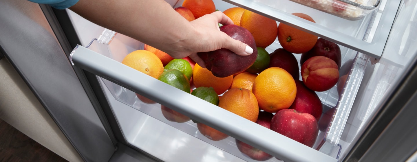 Crisper drawer filled with limes, peaches, oranges and apples Crisper drawer filled with limes, peaches, oranges and apples