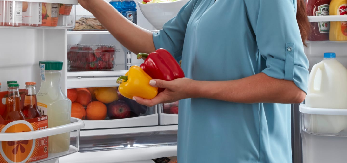 Person taking red and yellow peppers out of the fridge Person taking red and yellow peppers out of the fridge