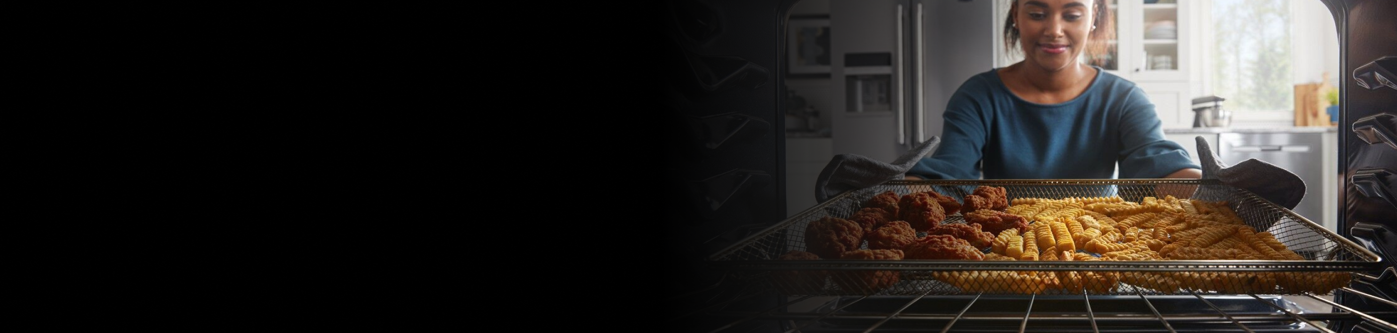 Person removing chicken strips and french fries from an oven