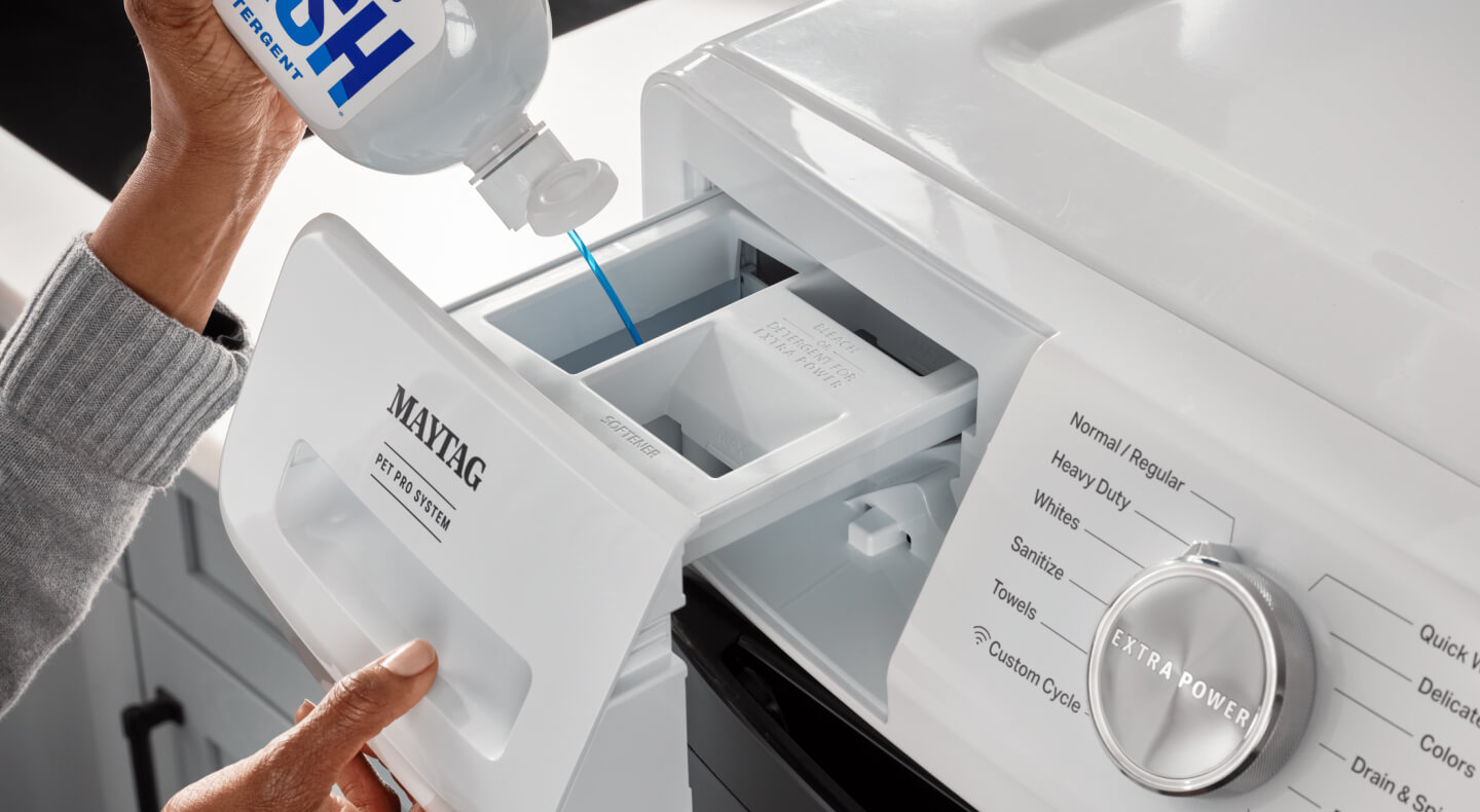 Hand dispensing detergent into a white Maytag® front load washer