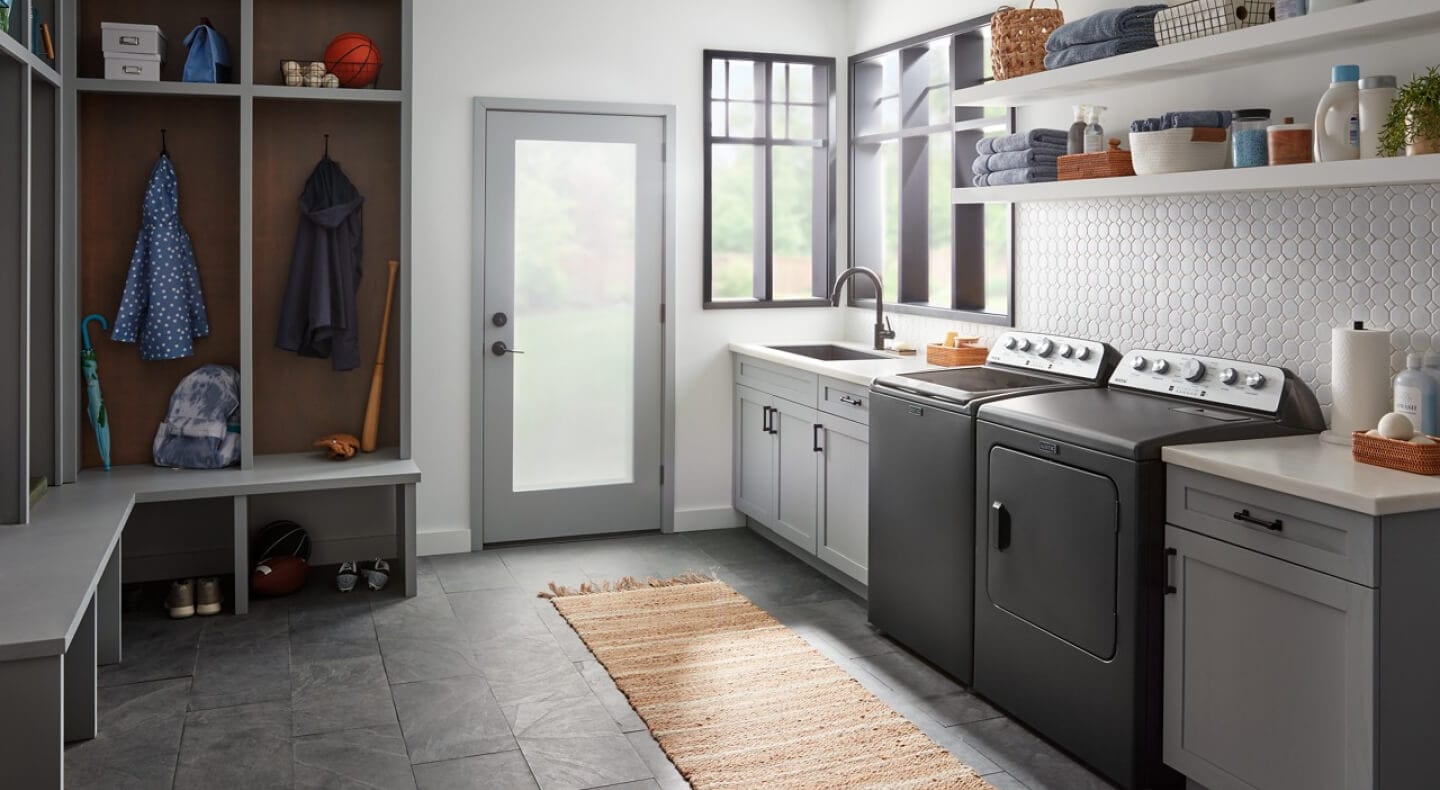 A black top load washer and dryer in a laundry room with gray floors, white shelving and grey locker cabinets