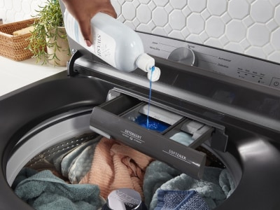 Person putting detergent into dispenser in top load washing machine