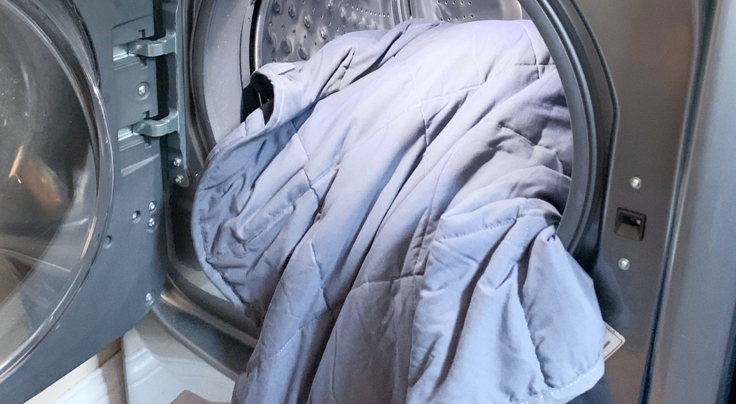 Pale blue comforter halfway inside of front load washing machine with door open Pale blue comforter halfway inside of front load washing machine with door open
