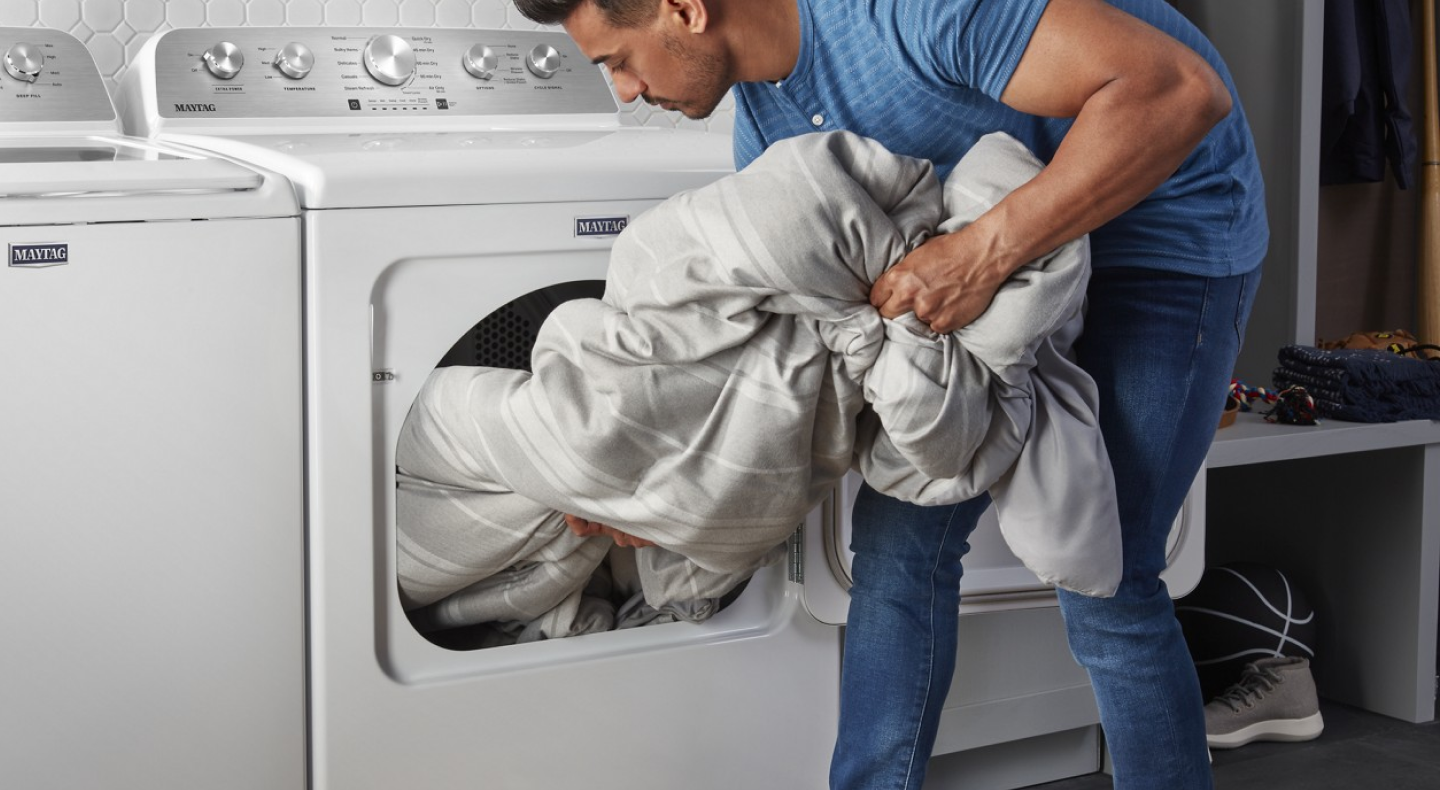 Person loading large white comforter into dryer
