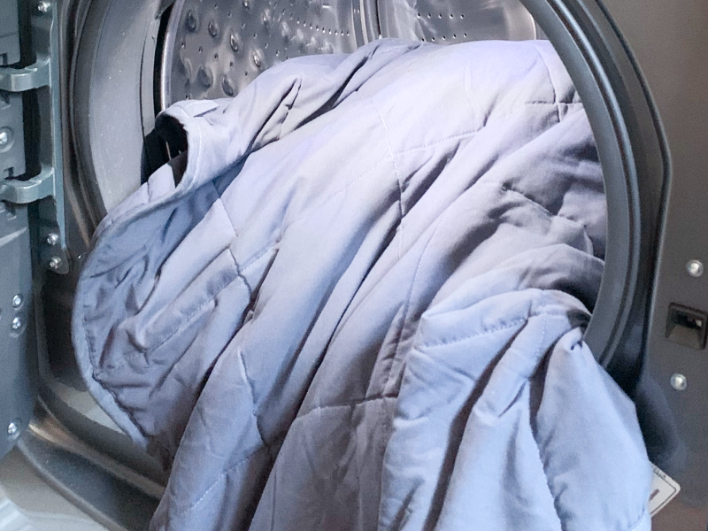 Pale blue comforter halfway inside of front load washing machine with door open Pale blue comforter halfway inside of front load washing machine with door open