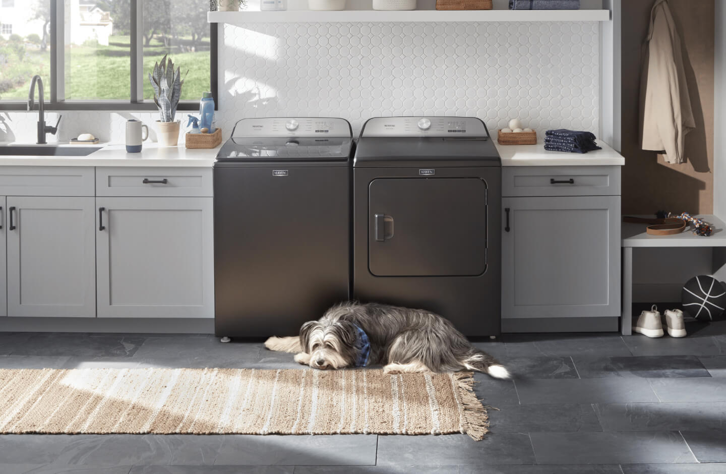 A Maytag® top load  washer and dryer pair in a laundry room with a dog laying in front