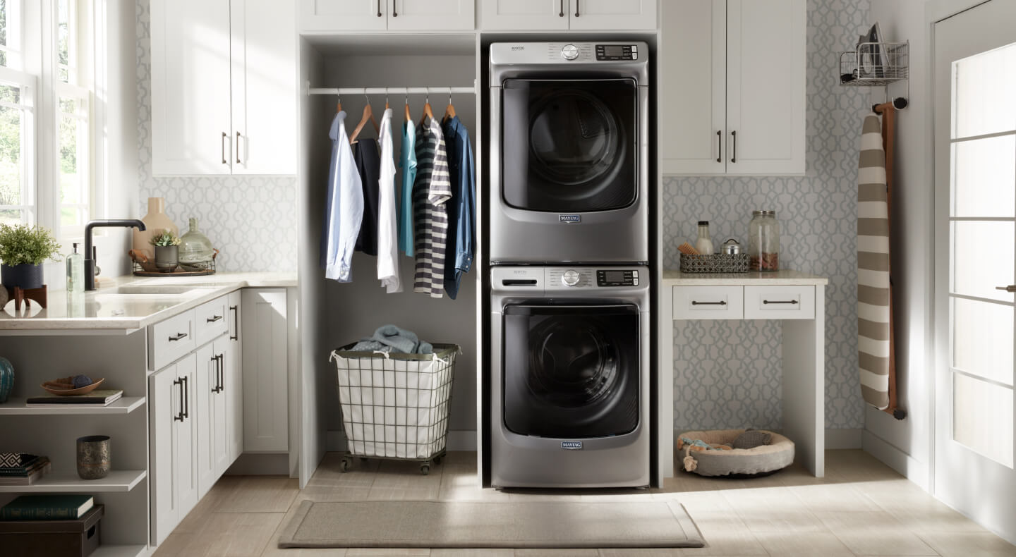 Stacked stainless steel front load washer and dryer in a laundry room with white cabinetry