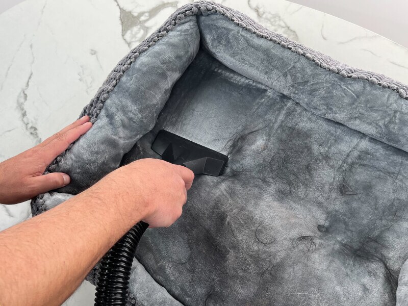 A person vacuuming off pet hair from a dog bed