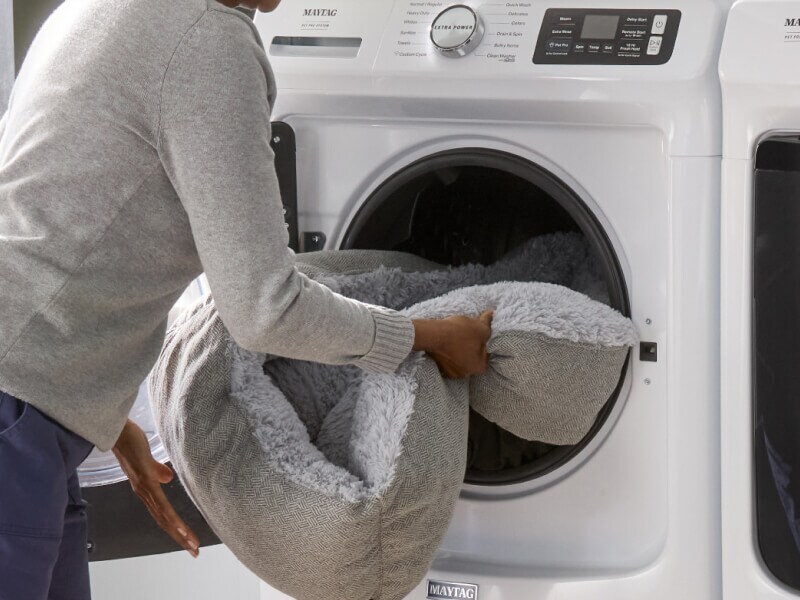 A person loading a dog bed into a washer